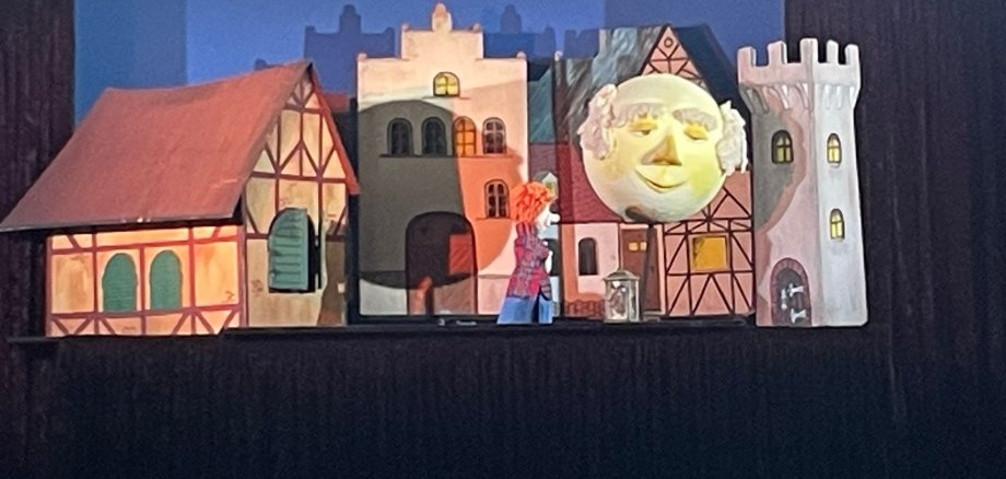 Сцената на кукления театър "Die Mondlaterne" с малки къщички и голяма луна.