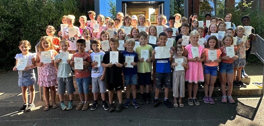 Children stand in front of the school building and present their certificates of honor.