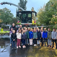 The children and the teacher of class 4b stand with Mr. Droste in front of the combine harvester.