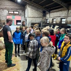 The children stand in the barn and listen to the farmer's explanations.