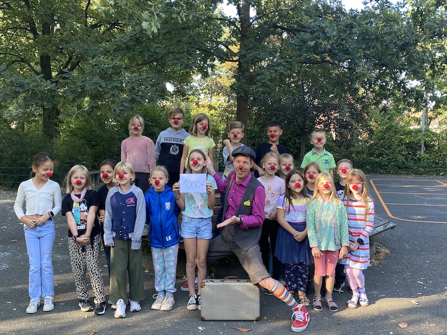 Los niños llevan narices rojas de payaso mientras entregan la donación a un payaso de la clínica.