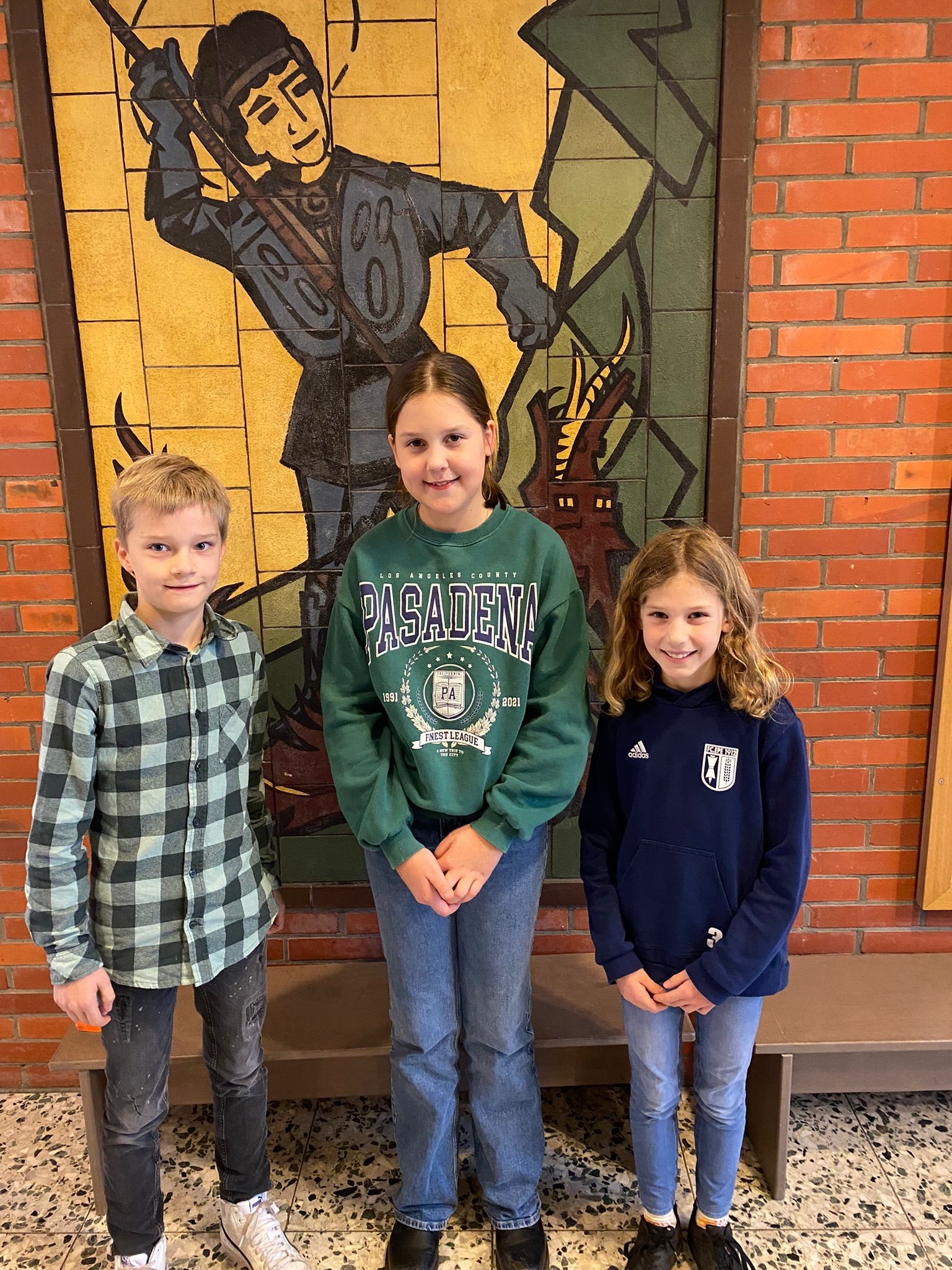 Lugemisvõistluse klassivõitjad Jonathan Nollmann (4c), Paula Klöpper (4a) ja Tilda Weinberg (4b) seisavad Püha Georgi mosaiigi ees.