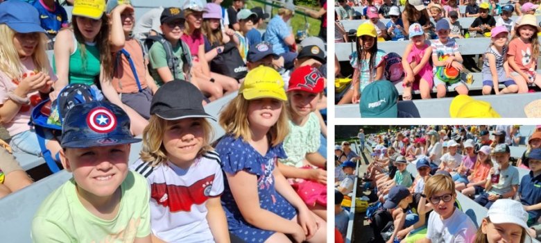 Des enfants assis en public sous le soleil, portant chapeaux et casquettes.