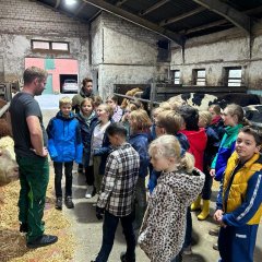 Les enfants sont dans l'étable et écoutent les explications de l'agriculteur.