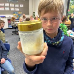 Un enfant tient en l'air un pot à vis avec une motte de beurre.