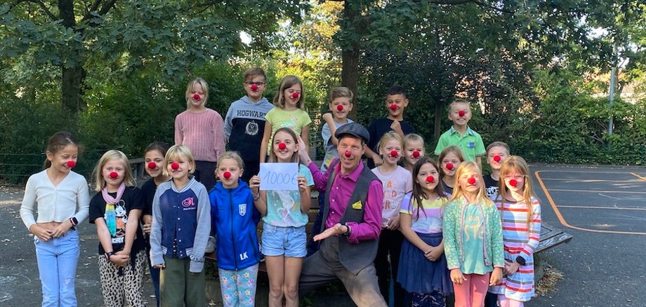 De kinderen dragen rode clownsneuzen terwijl ze de donatie overhandigen aan een clown van de kliniek.