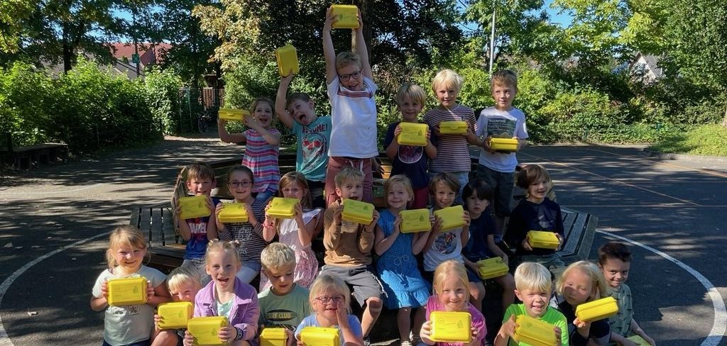De kinderen van de Punguin klas houden hun nieuwe brooddozen omhoog en lachen in de camera.